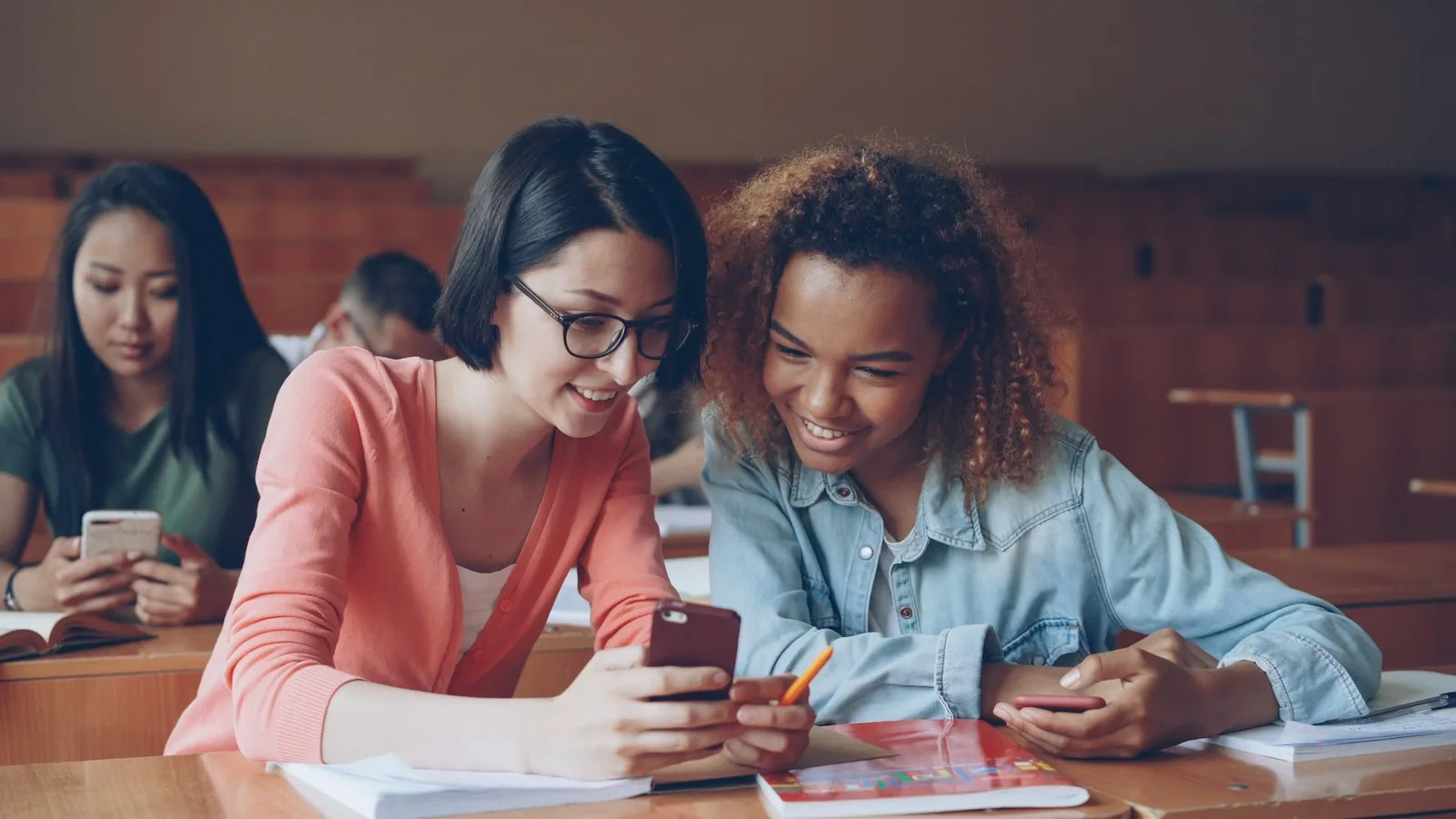 Two university students talking together at their desks in class