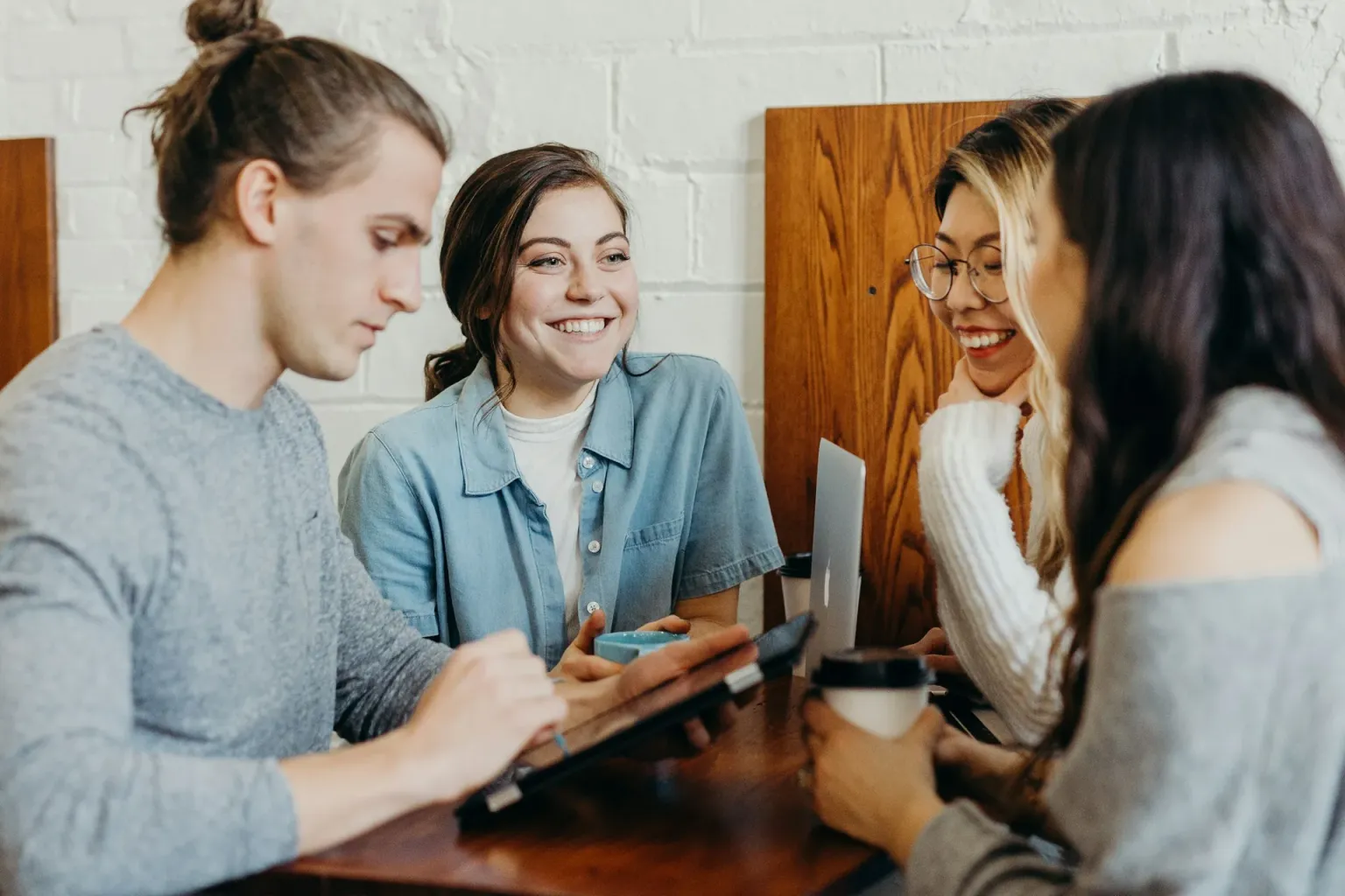 A group of friends laughing together around a table with laptops and coffee