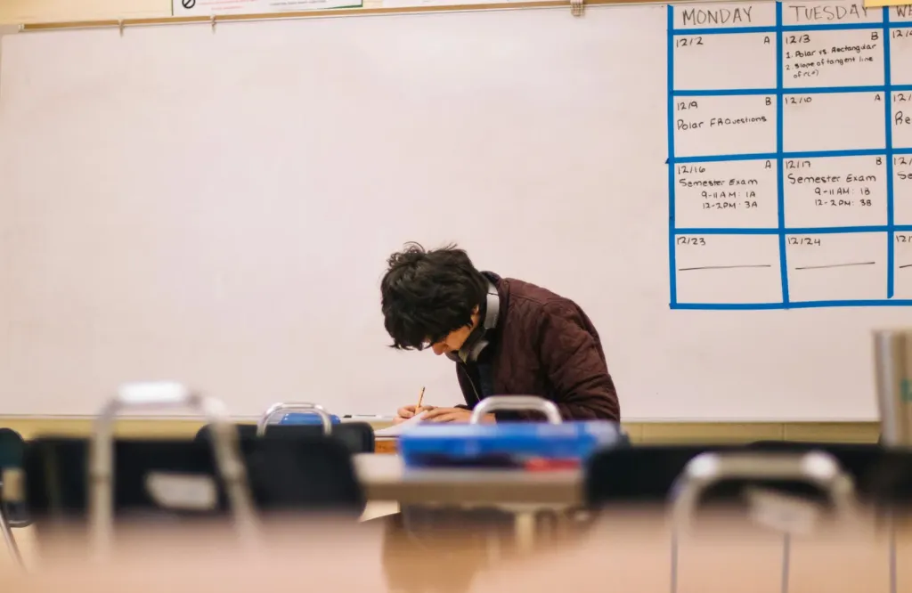 A student alone at a classroom desk, head down, working through an assignment