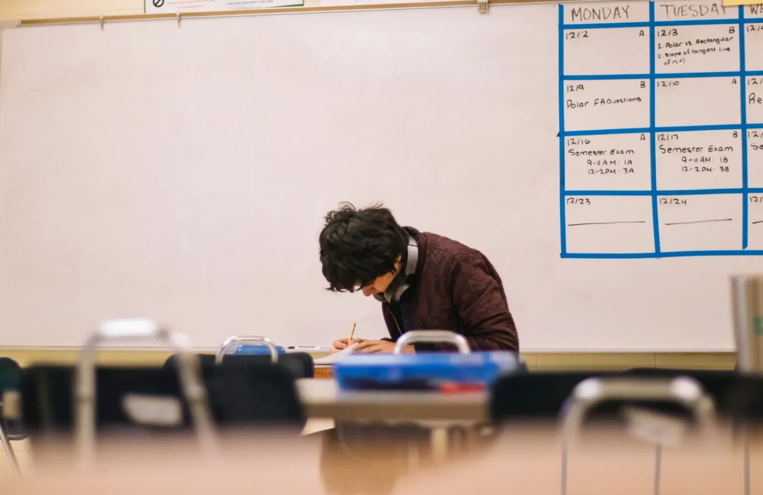A student alone at a classroom desk, head down, working through an assignment